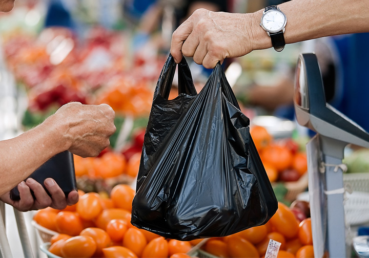 A black plastic bag is handed from one person to another in the fruit and vegetable section of a supermarket. 