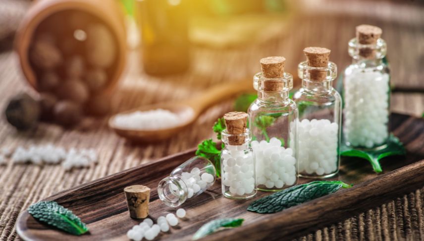 Homeopathic remedy pellets in glass vials arranged on a wooden tray.