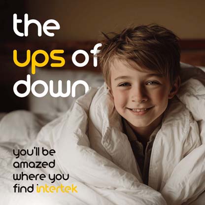 A boy smiling while sitting in bed wrapped in a down comforter